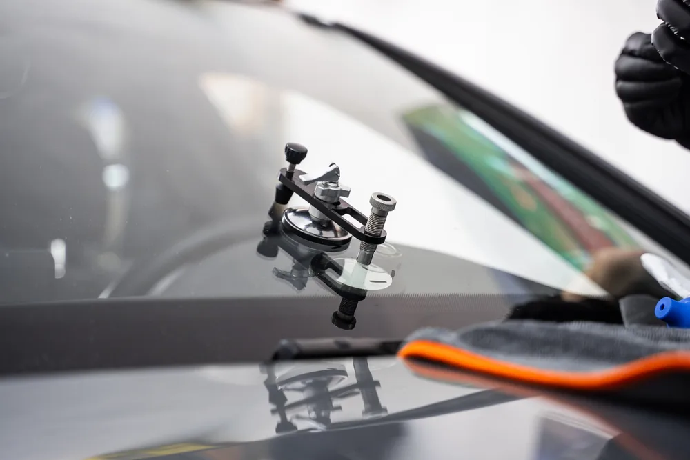 Gloved technician using a professional resin-injection tool on a windshield chip