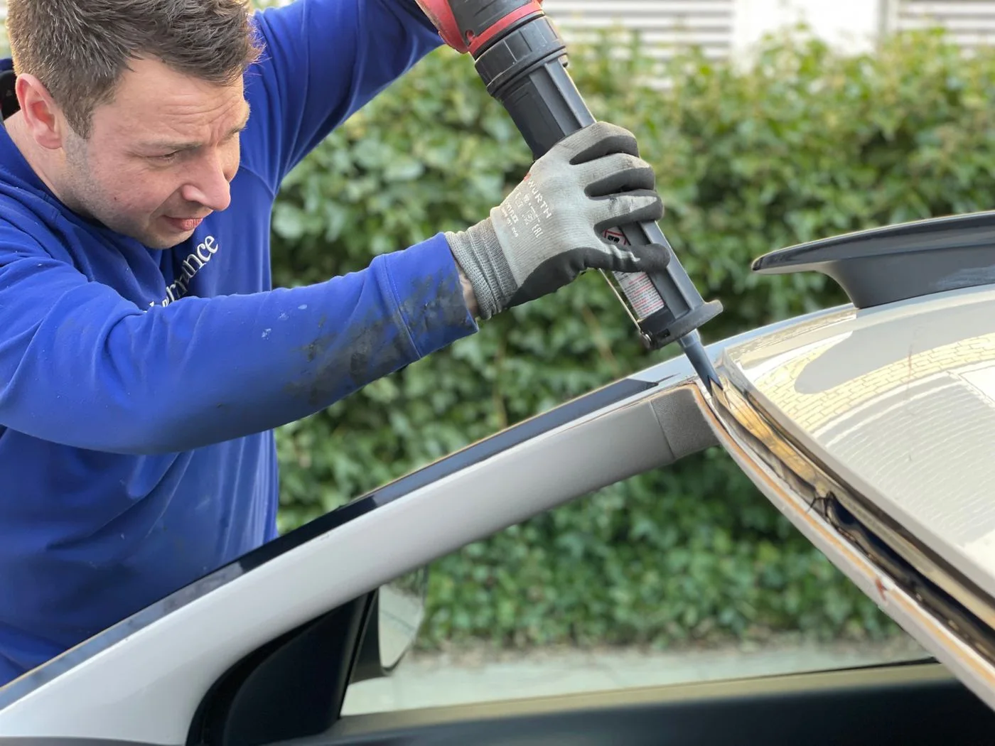 Mobile automotive glass technician working on a vehicle outdoors with professional tools